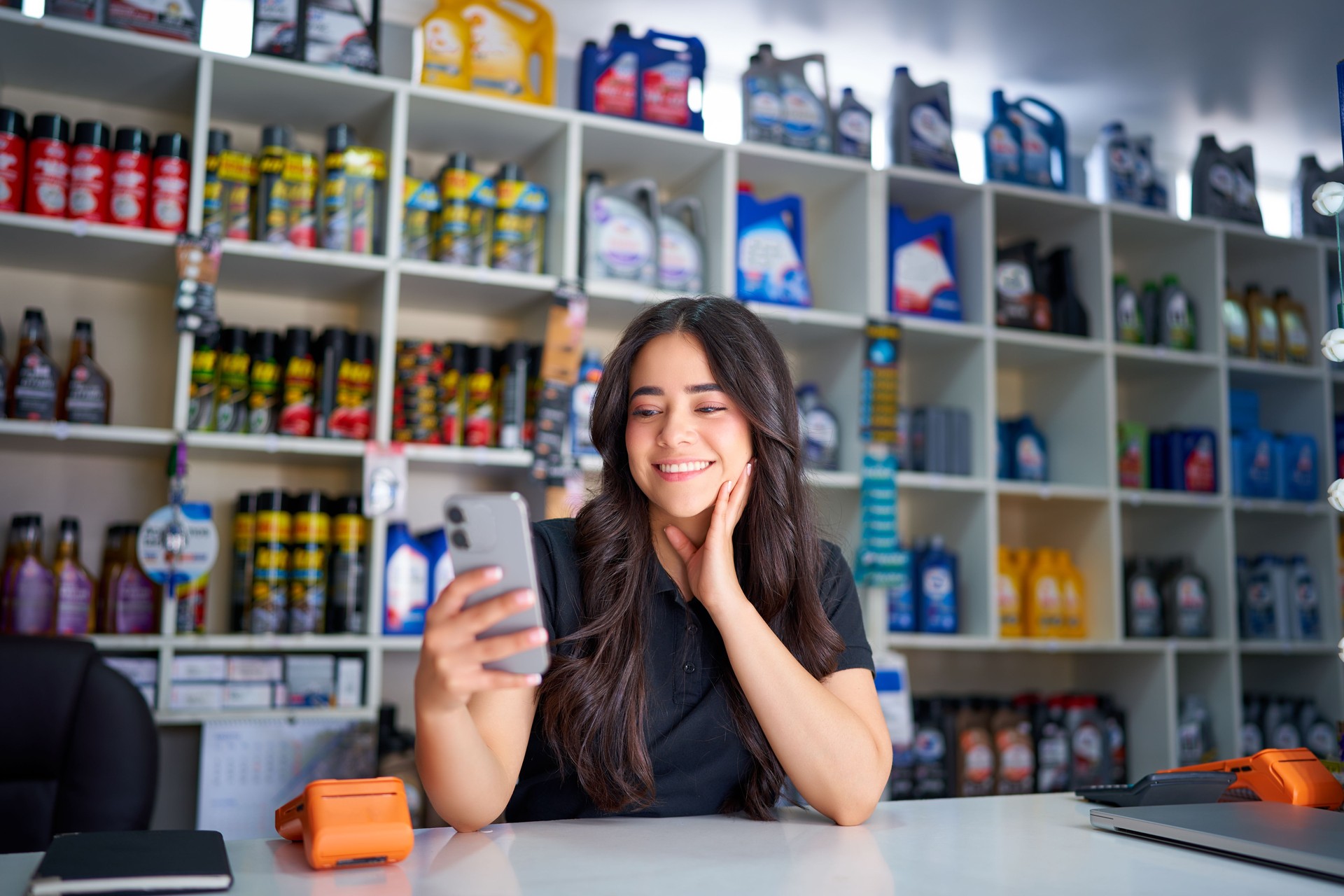 Latina saleswoman holding and looking at smartphone in auto parts store